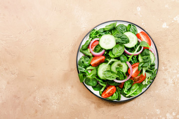 Spring vegan salad with spinach, cherry tomatoes, corn salad, baby spinach and red onion. Healthy food concept. Beige stone table.Top view. Copy space