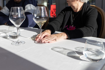 a wine glass in old hands, white wine in wine glass in a restaurant, elderly woman with wine