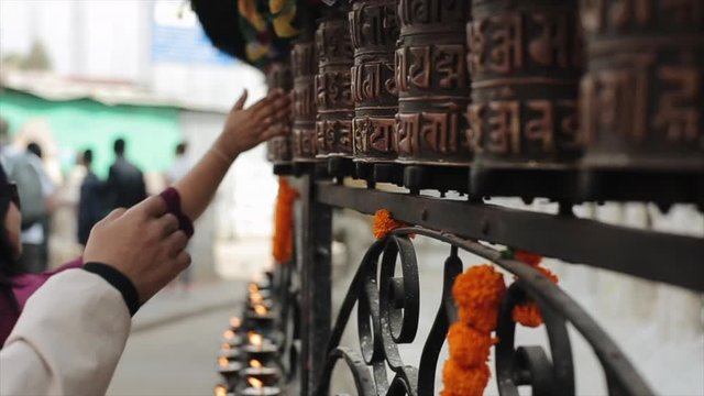 A close-up view of nepalese people spinning prayer wheels. Kathmandu Nepal. Hands. Candles and prayer flags in the background.