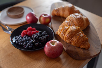 Big croissants, berries, red apples on a wooden table