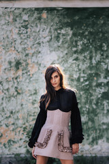 Fototapeta premium Pretty brunette Model in a designer dress posing at camera on spring day on the old wall background
