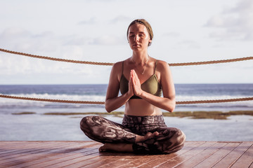 Young attractive girl sitting on wooden floor, practicing yoga and pranayama. Lotus pose. Calm...