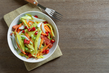 top view of spicy mango salad in a ceramic bowl on wooden table. asian homemade style food concept.