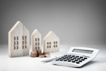Calculator with wooden house and stack of coins
