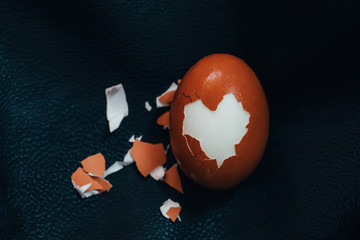 Cracked hard boiled brown egg with heart shaped shell on black leather background. Minimal Easter holiday concept. - Powered by Adobe