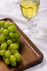 Close up of green grapes on a wooden serving board. With white wine in wine glass.