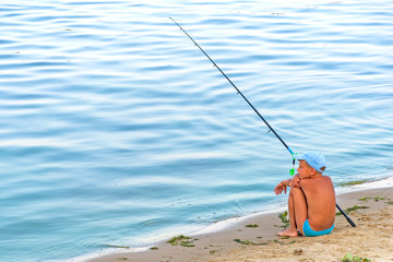 Fototapeta na wymiar Boy with fishing rod sitting near the lake