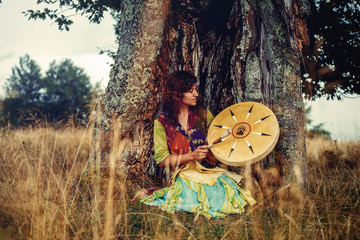 beautiful shamanic girl playing on shaman frame drum in the nature.