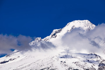 Snowy summit of Mount Hood with clouds and blue sky. Mt Hood National Park, Oregon, USA.