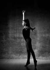 Young girl gymnast in black sport body and special uppers standing and making gymnastic pose over dark background