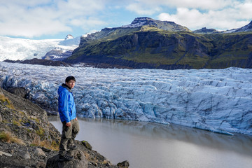 Young Asia man standing on the rock looking view of glacier at svinafellsjokull, iceland