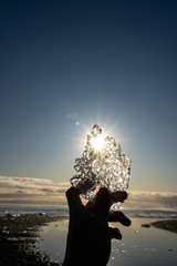 Silhouette crystal ice piece break holding by hand with sun star on ice hold in afternoon time Diamond beach Jokulsarlon, Iceland