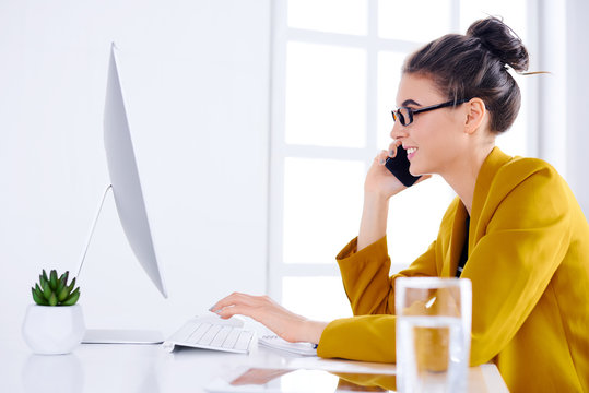 Young business woman talking on the phone while using desktop