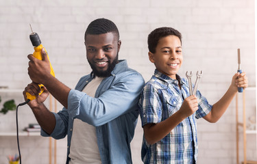 Happy black father and son posing with construction tools at home