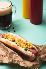 hot dog with corn, glass of beer and bottles with mustard and ketchup on blue