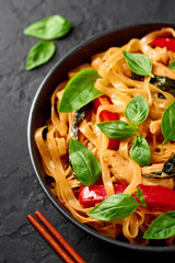 Thai Drunken Noodles or Pad Kee Mao in black bowl at dark slate background. Drunken Noodles is thai cuisine dish with Rice Noodles, Chicken meat, Basil, sauces and vegetables. Thai Food. Close up