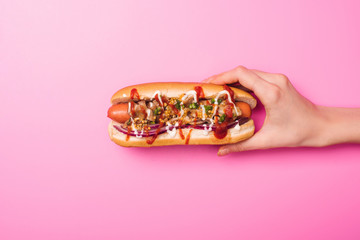 partial view of woman holding one tasty hot dog on pink