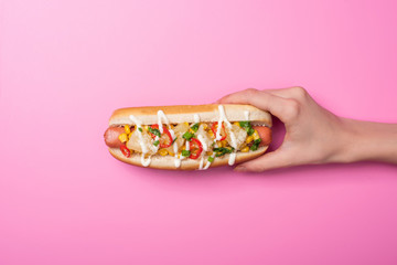 cropped view of woman holding tasty hot dog on pink