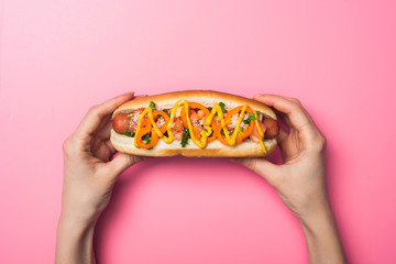 cropped view of woman holding yummy hot dog with mustard on pink
