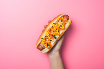 cropped view of woman holding delicious hot dog on pink