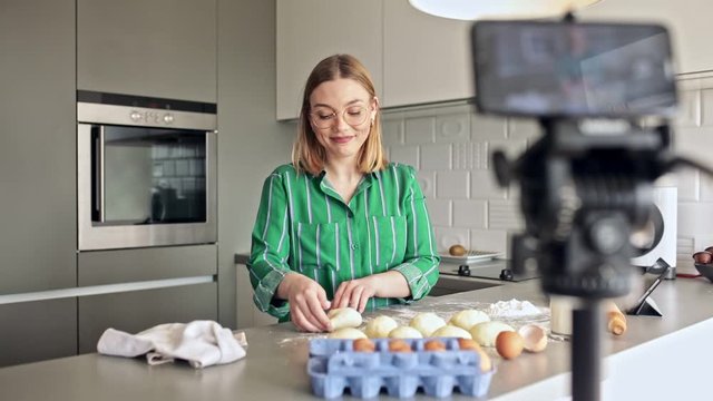 Young woman recording vlog at home in the kitchen preparing dough for pasta.