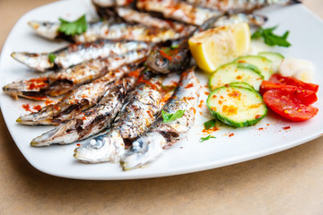 Fresh Grilled sardines served with fresh tomatoes, cucumbers slices and lemon on white plate for mediterranean healthy meal