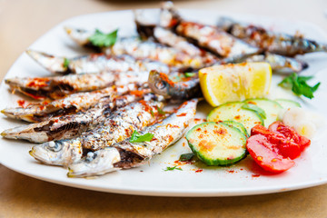 Fresh Grilled sardines served with fresh tomatoes, cucumbers slices and lemon on white plate for mediterranean healthy meal