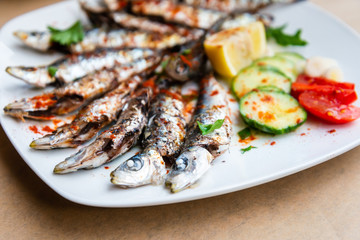 Fresh Grilled sardines served with fresh tomatoes, cucumbers slices and lemon on white plate for mediterranean healthy meal