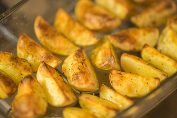 Ready golden baked potato slices in glass dish after oven.