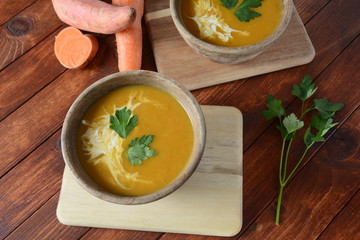 Sweet potato and carrot soup served with sour cream in wooden bowl. Orange vegetable soup concept. Vegan food