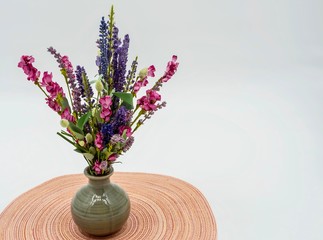 Pink and Purple artificial wildflowers in a gray ceramic vase sitting on a round pink and white placemat with a white background.