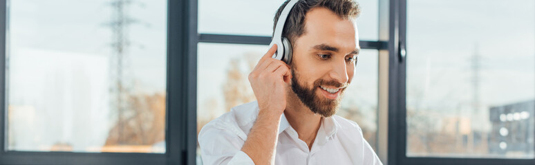 panoramic shot of professional smiling translator working online with headphones and laptop