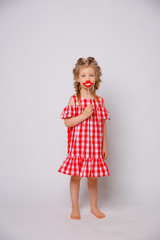 Funny smiling baby girl in a summer dress on a white background full-length . Baby girl with a lip accessory on a stick.