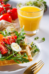Healthy breakfast - homemade waffles, egg and fresh organic tomatoes salad with orange juice glass on a light grey background.