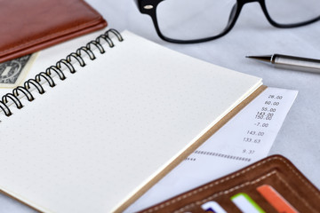 Close-up view, Blank notebook for daily expenses with wallet, bill, pencil and glasses is elements.