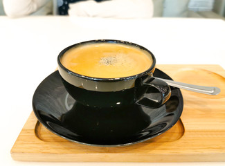 black coffee cup on wood tray, on white table and blur woman sitting opposite