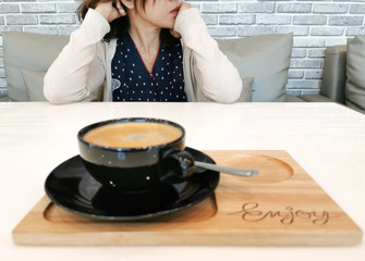 black coffee cup on wood tray, on white table and blur woman sitting opposite