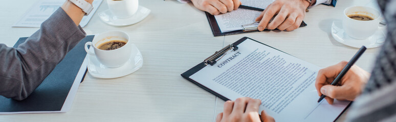 panoramic shot of businesspeople with contract and coffee cups on meeting in office