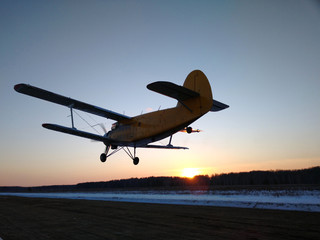 Fototapeta na wymiar old biplane plane on takeoff after taking off from the runway rear view of a winter landscape at sunset with a cloudless sky