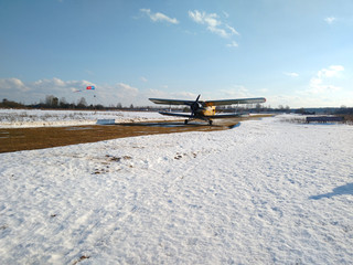 Yellow old biplane plane on a dirt runway in winter on a Sunny day with blue sky and white snow