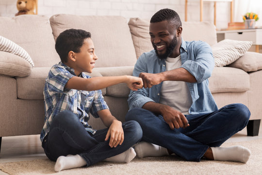 Cheerful Black Preteen Boy Fist Bumping With His Dad At Home