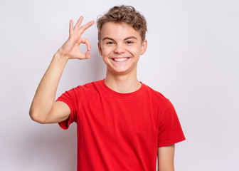 Portrait of teen boy making Ok gesture on grey background. Handsome caucasian young teenager smiling and giving OK sign. Happy cute child showing okay.