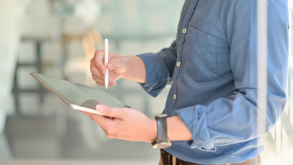 Two young businessmen consulted about their work by using a tablet while standing at working place, Side view image.