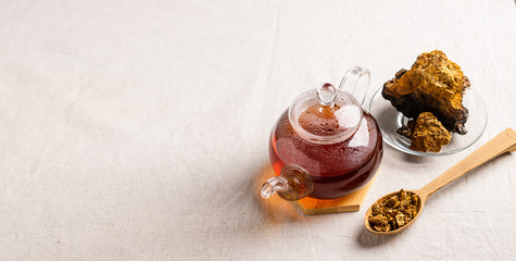 Wellness tea from chaga tree mushroom in a glass teapot and glass. Organic drink antioxidant gray natural background.