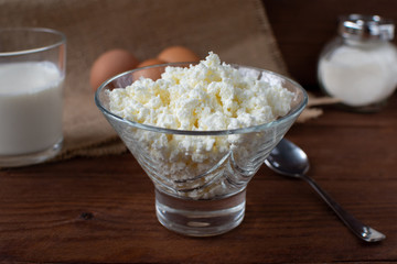 Homemade rustic crumbly cottage cheese with milk on a wooden background. Still-life.