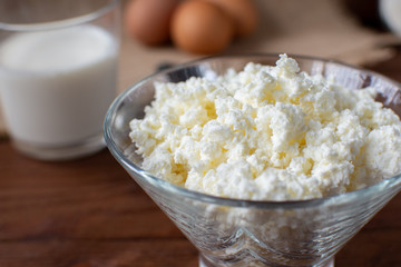 Homemade rustic crumbly cottage cheese with milk on a wooden background. Still-life.