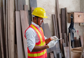Handsome man wearing safety vest and yellow helmet,holding tablet in hand,for checking wood work at factory,blurry light around