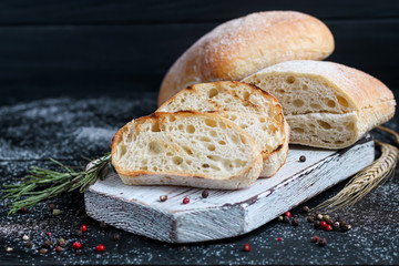 Ciabatta with rosemary, olive oil and cherry tomatoes on a wooden board. On a dark background.