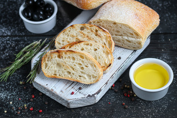 Ciabatta with rosemary, olive oil and cherry tomatoes on a wooden board. On a dark background.