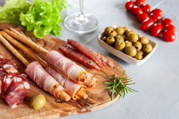Set of smoked bacon, salami and basturma served with pickled olives, tomatoes, wine and grissini bread. Close up on white background
